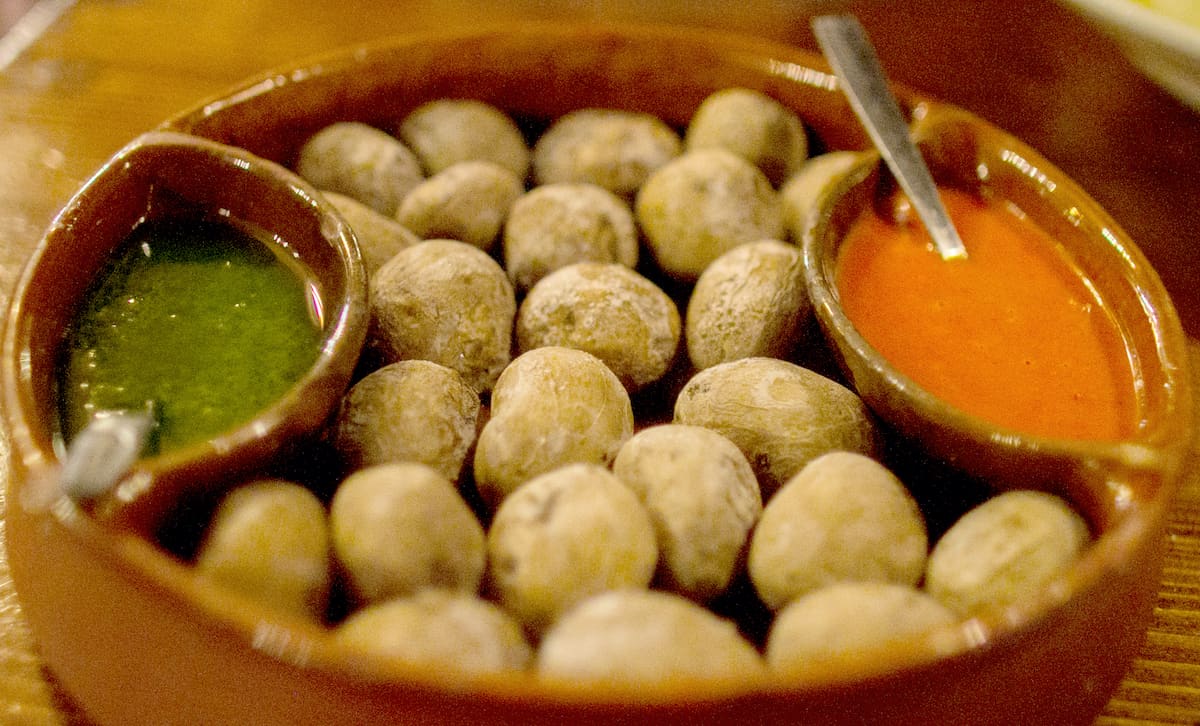 Clay dish of small whole potatoes with a red sauce and a green sauce