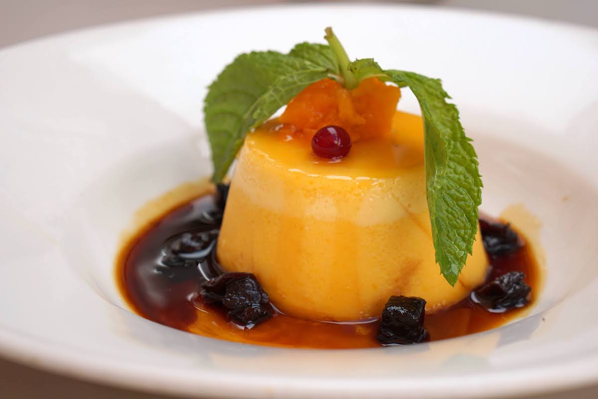 Flan garnished with herbs and berries in a white dish