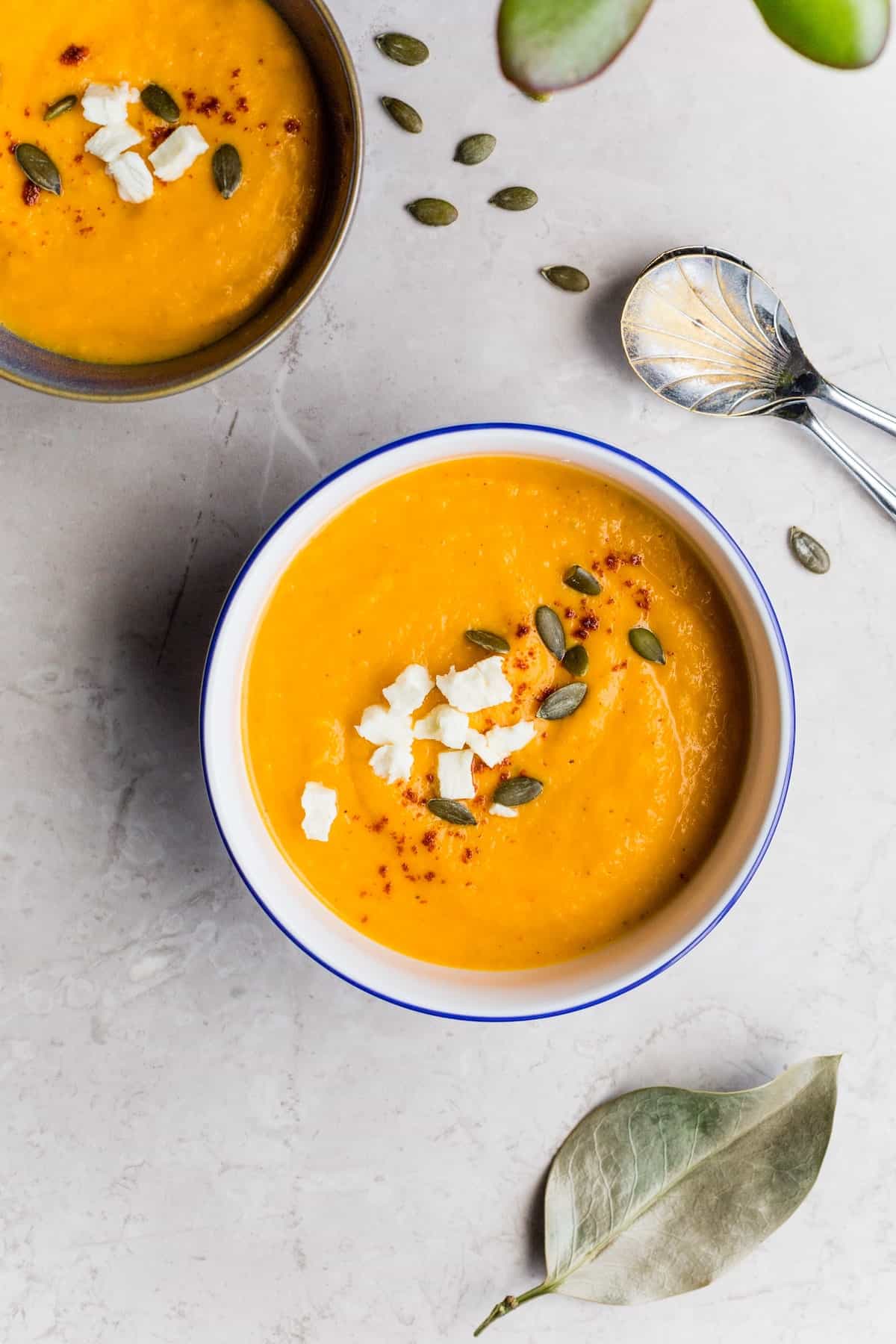 Overhead shot of two bowls of pumpkin soup topped with soft cheese and pepitas