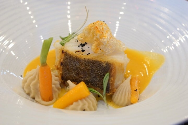 Close-up of a small piece of salt cod with several intricate garnishes and an orange sauce.