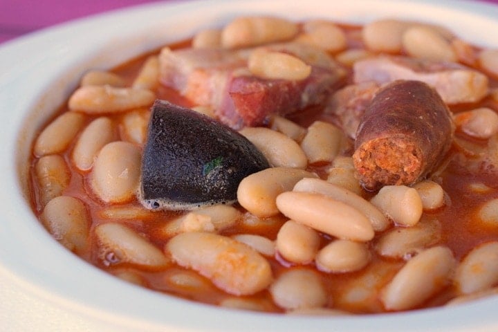 Close-up of a bowl of fabada: white bean stew with chorizo, blood sausage, and pork fat.