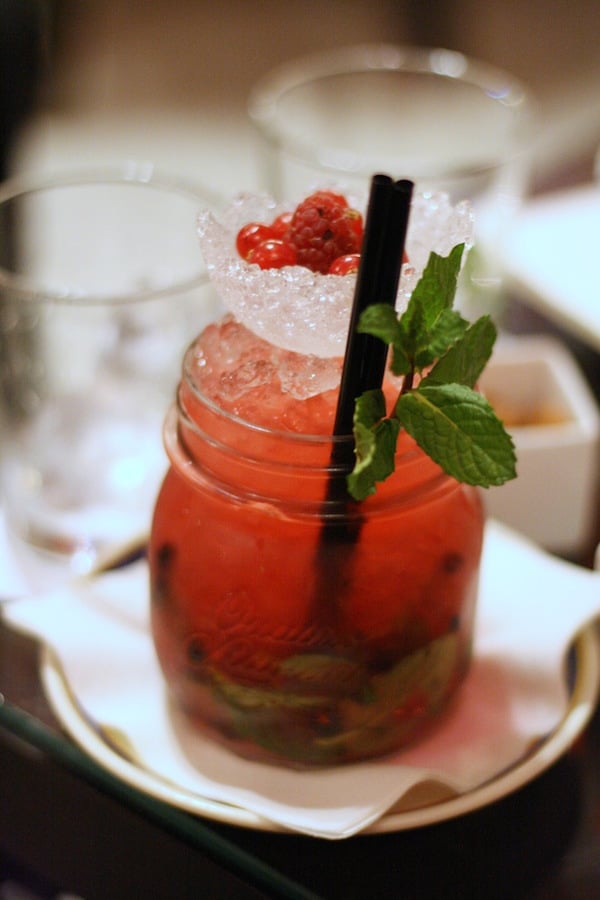 A bright red cocktail in a glass jar with crushed ice, fresh mint, and red berries.