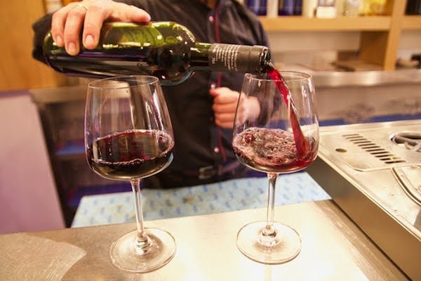 Close-up of a waiter pouring red wine into a glass, with a full glass beside it.