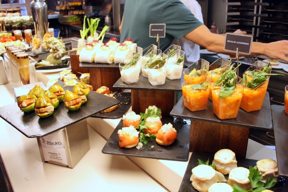 An array of colorful pintxos set out on slate serving boards atop a bar