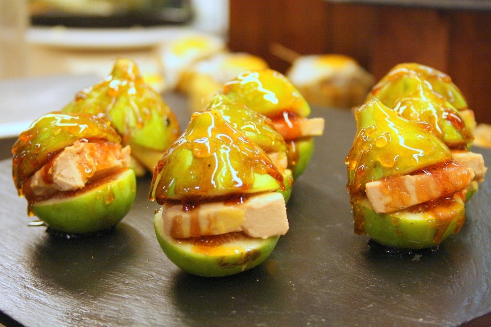 A plate of fresh green figs sliced in half, stuffed with cheese, and drizzled with honey. 