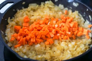 Carrots on top on onions frying in a skillet