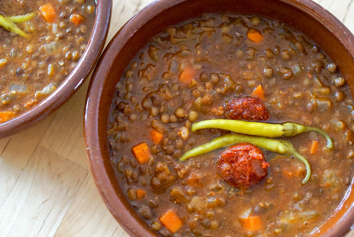 Spanish lentils with chorizo and pickled peppers in clay bowls.