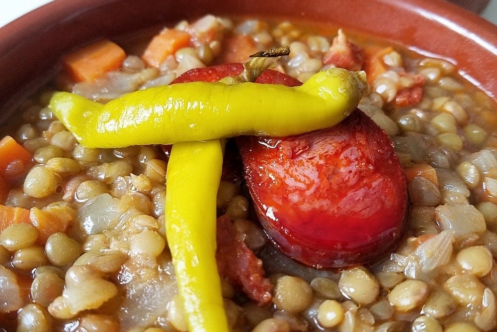 Close-up of a bowl of lentil stew with chorizo and bright yellow pickled peppers.