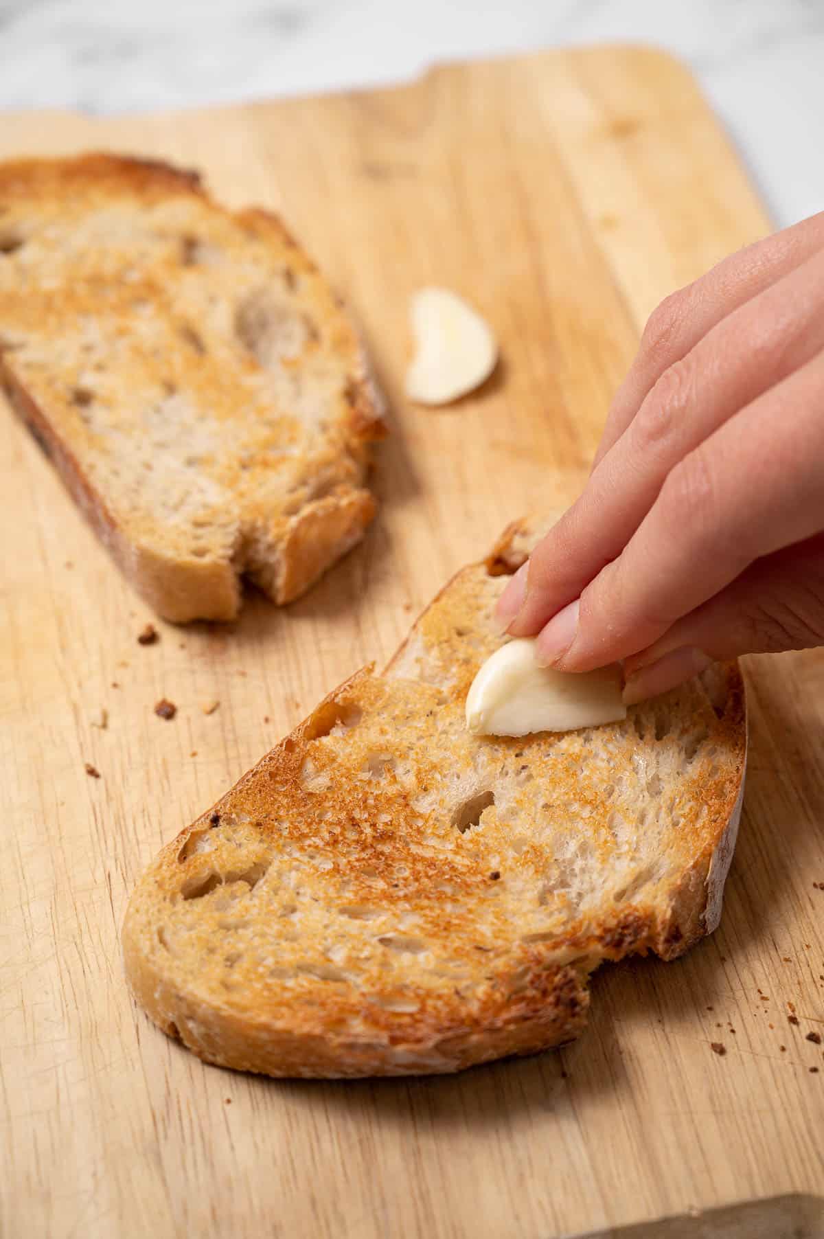 Close-up of someone rubbing a garlic clove on toasted bread to make Catalan tomato bread.