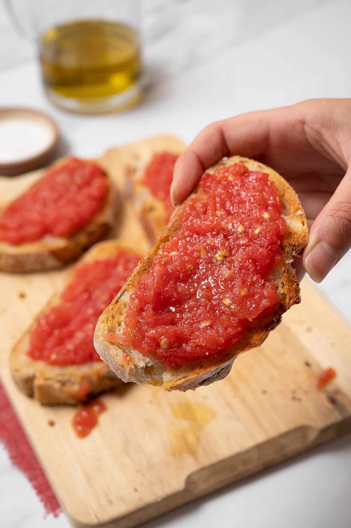 A hand holding a slice of Pan con tomate