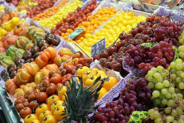 A market display of brightly colored fruits in bins, including various kinds of tomatoes and grapes.