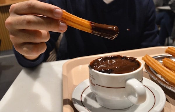 Close-up of someone holding a churro that's been dipped into a cup of thick hot chocolate.