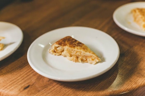 A slice of Spanish omelet on a white plate, with a gooey center and golden-brown top. 