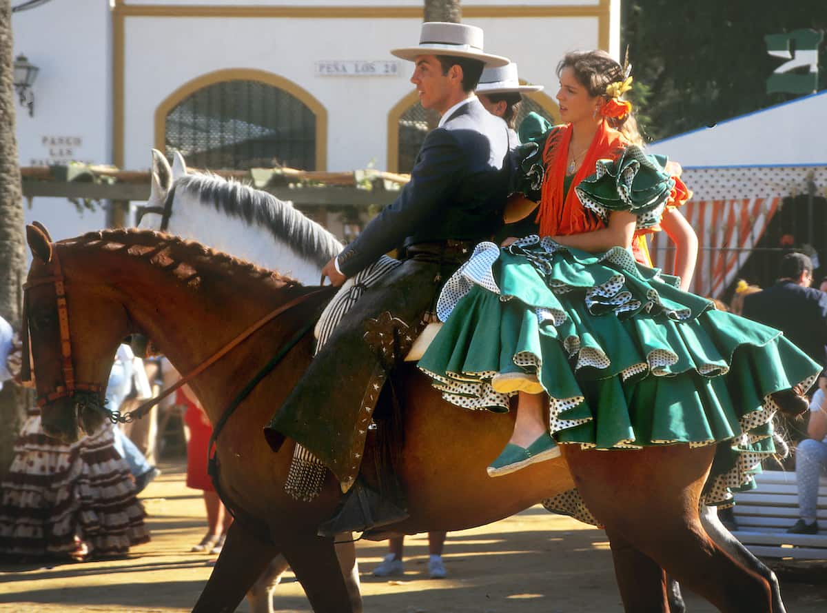 A couple in traditional Andalusian dress riding on horseback.