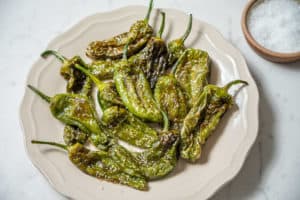 Plate of fried padron peppers with salt on the side.