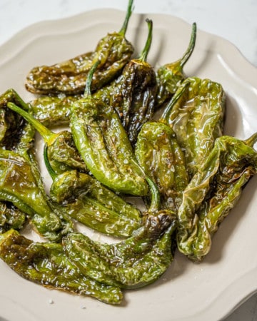 Plate of fried padron peppers with salt on the side.