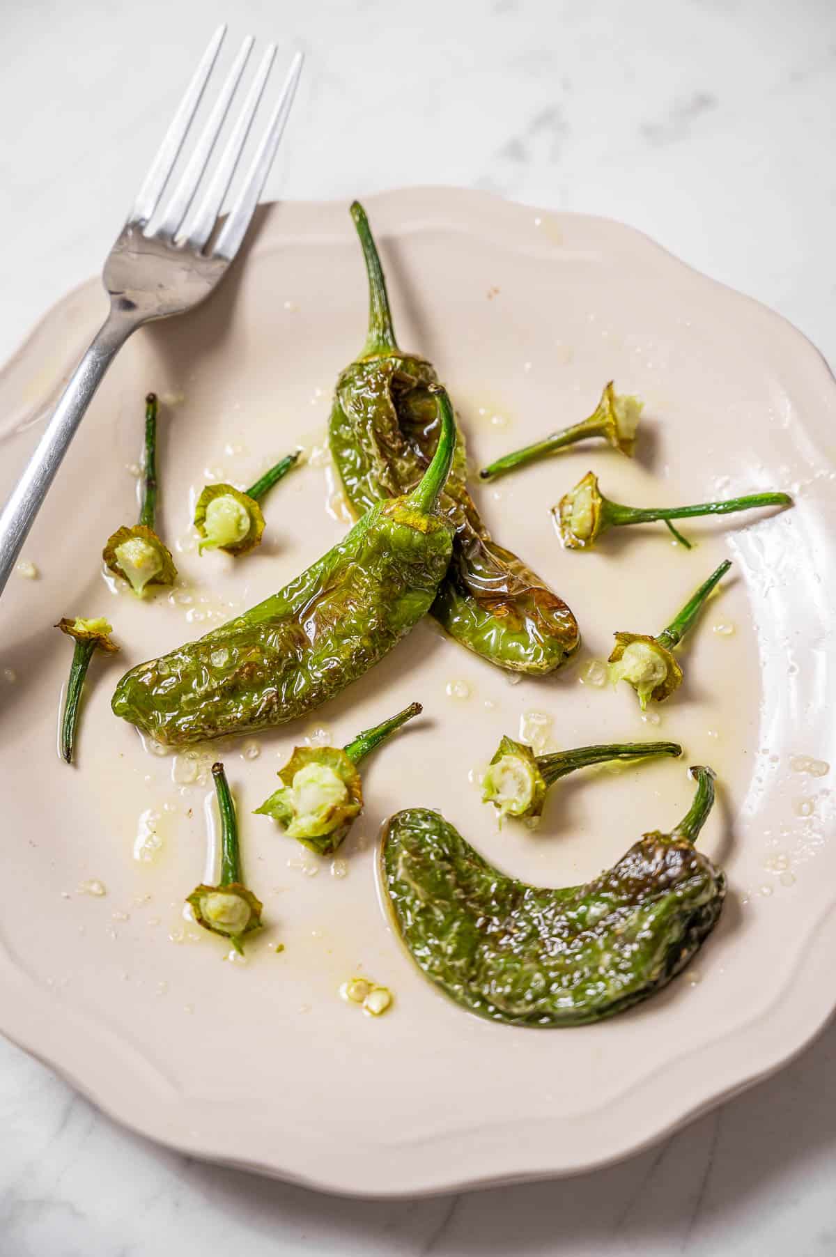 A plate of padron pepper stems and a few whole peppers. A half eater plate with a fork on top.