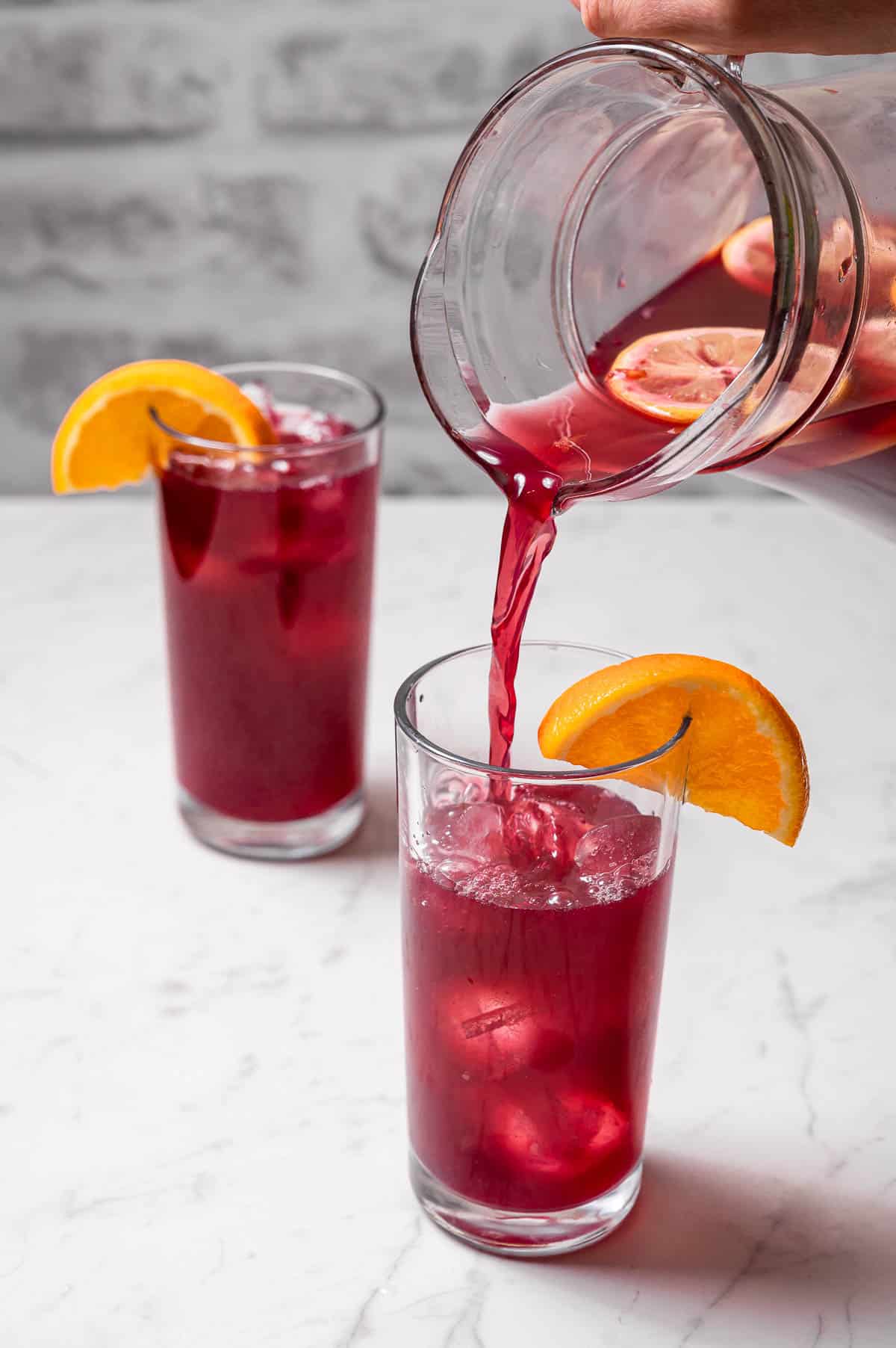 Two tall glasses of Spanish tinto de verano and a clear pitcher pouring more into one of them. 