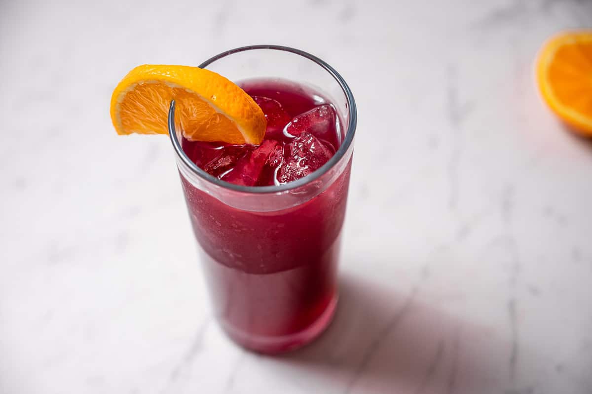 A tall glass of dark pink tinto de verano with an orange slice on the rim.