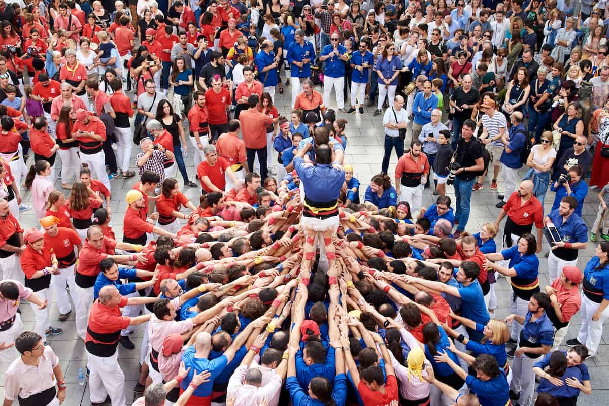 A group of castellers dressed in red and blue building a human tower in Barcelona.