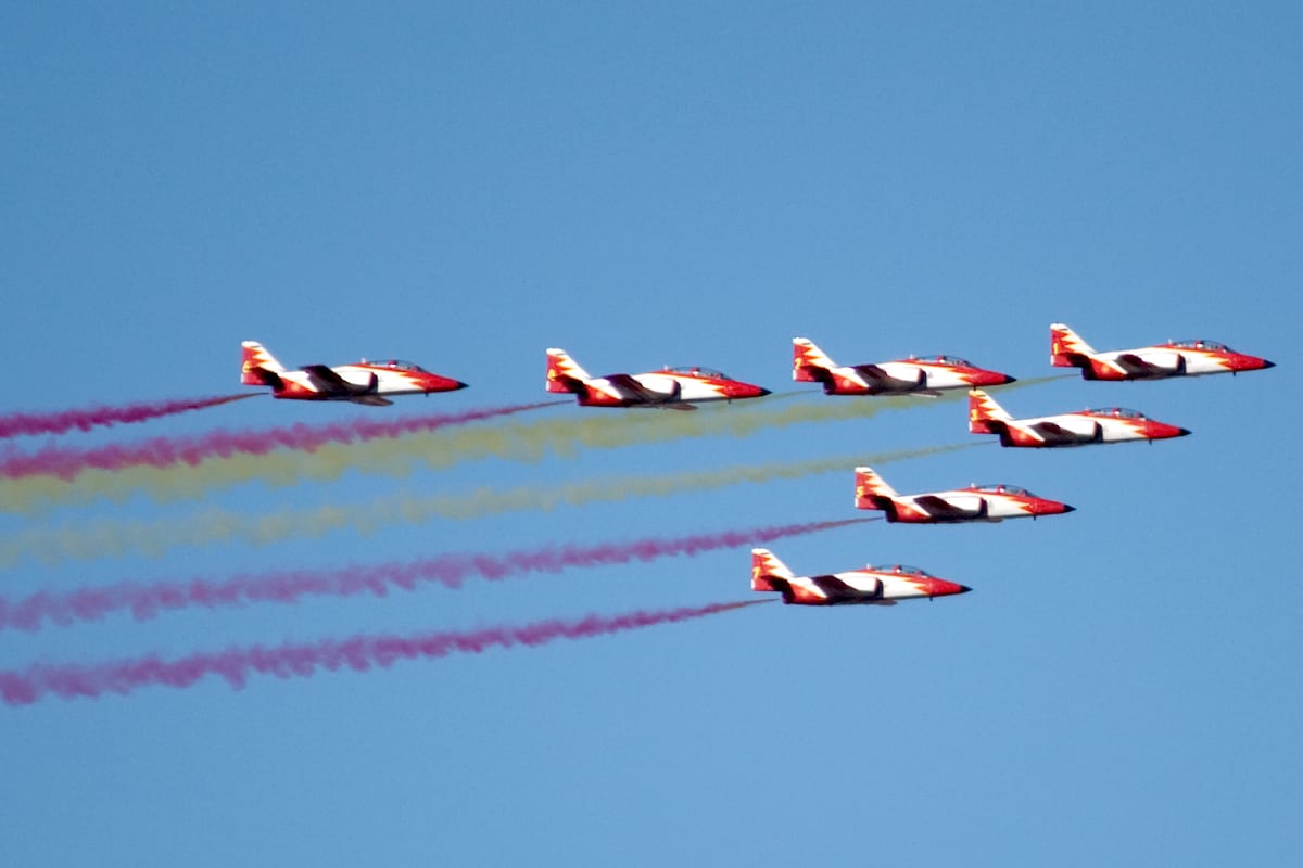 Seven jets in V formation releasing red and yellow smoke as they fly.