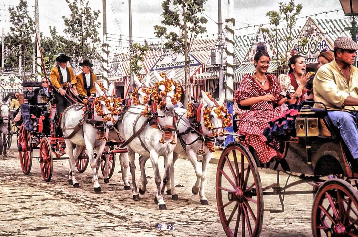 A group of people in traditional southern Spanish clothing riding in open horse drawn carriages.