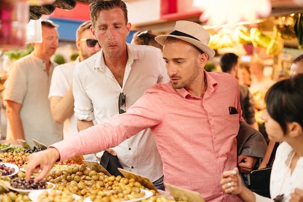 A man reaches out to pluck an olive from a bowl at a market stall.