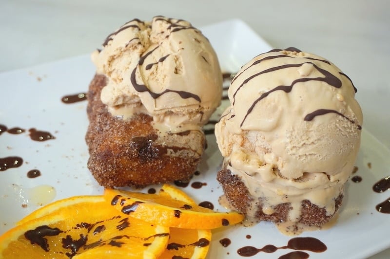 Two pieces of leche frita (Spanish fried milk) topped with ice cream and chocolate sauce.