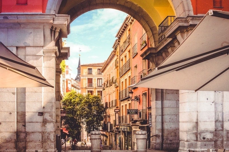 A view of Madrid's colorful historic buildings through the stone archway of one of its plazas.