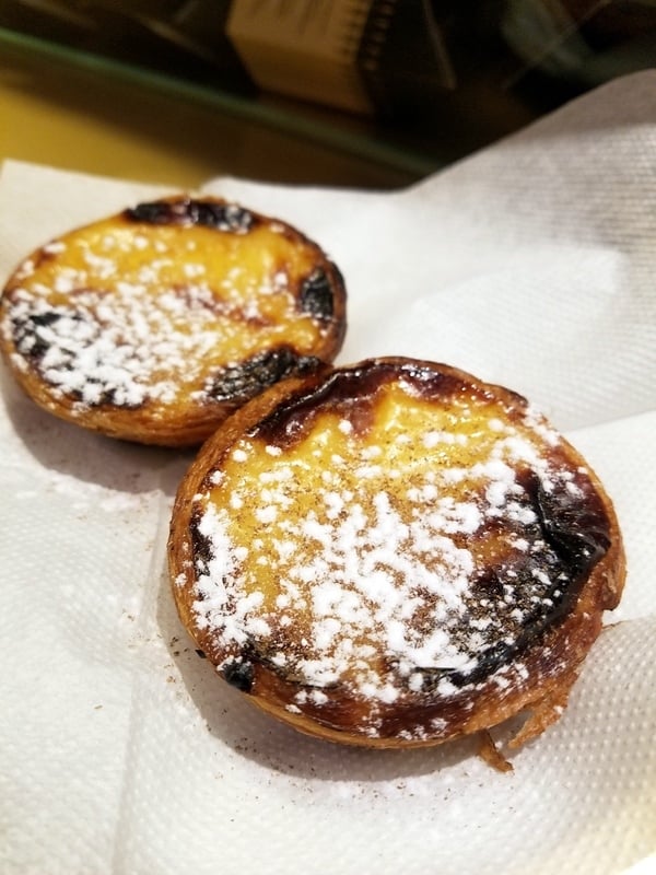 Close-up of two custard tarts on a napkin, dusted with lots of powdered sugar.