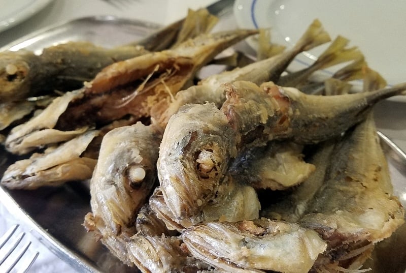 Close-up of fried whole sardines on a metal plate.