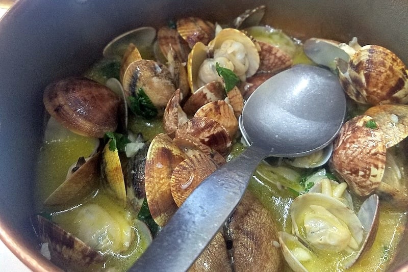 Close-up of a bowl of clams cooked in butter and garlic with a large spoon.