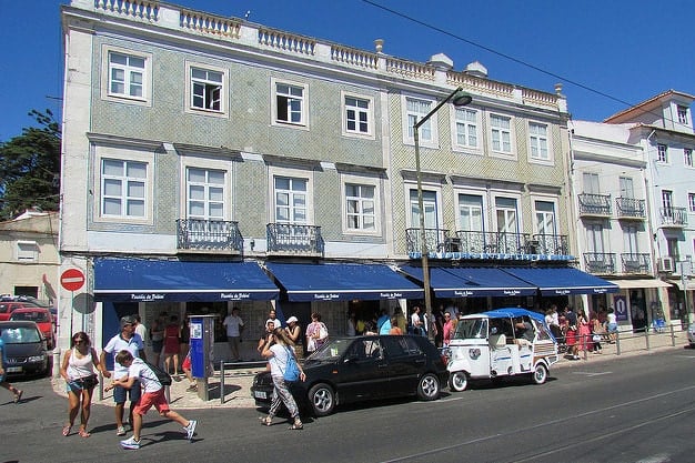 An old building with balconies and blue awnings and lots of people lined up outside.