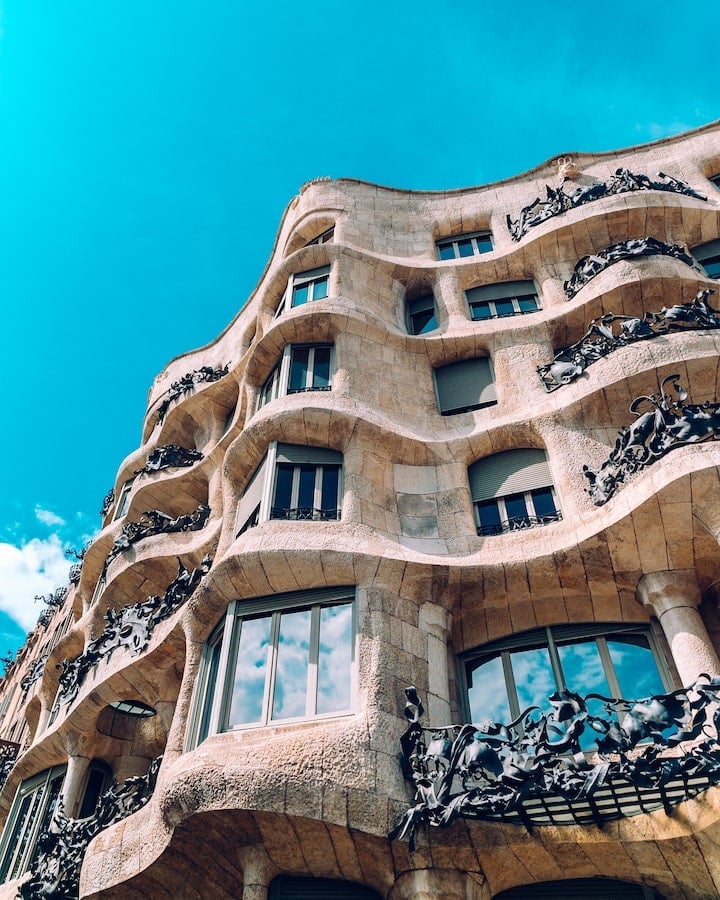 The undulating facade of a Barcelona building by Gaudí, with blue sky reflected in its windows.