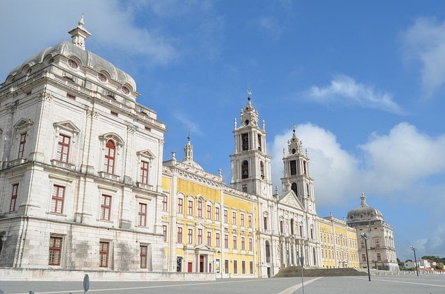 Wide view of Mafra National Palace, with white-and-yellow walls, red trim, and two towers.