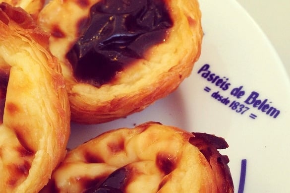 Close-up of three custard tarts on a plate reading "Pastéis de Belém: desde 1837."