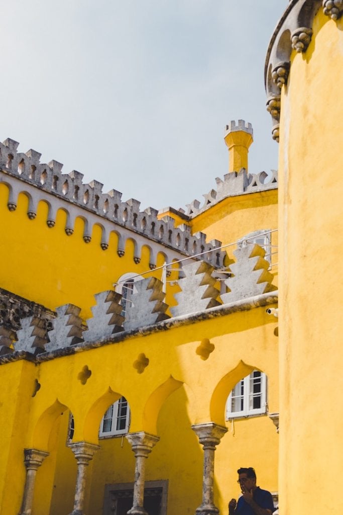 The bright yellow exterior walls of the Pena Palace, with elaborate stone battlements and cut-outs.