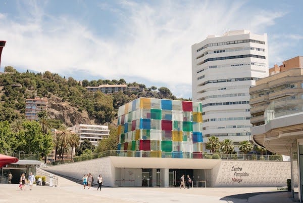 A low white building with a large cube covered in colorful translucent squares on top.