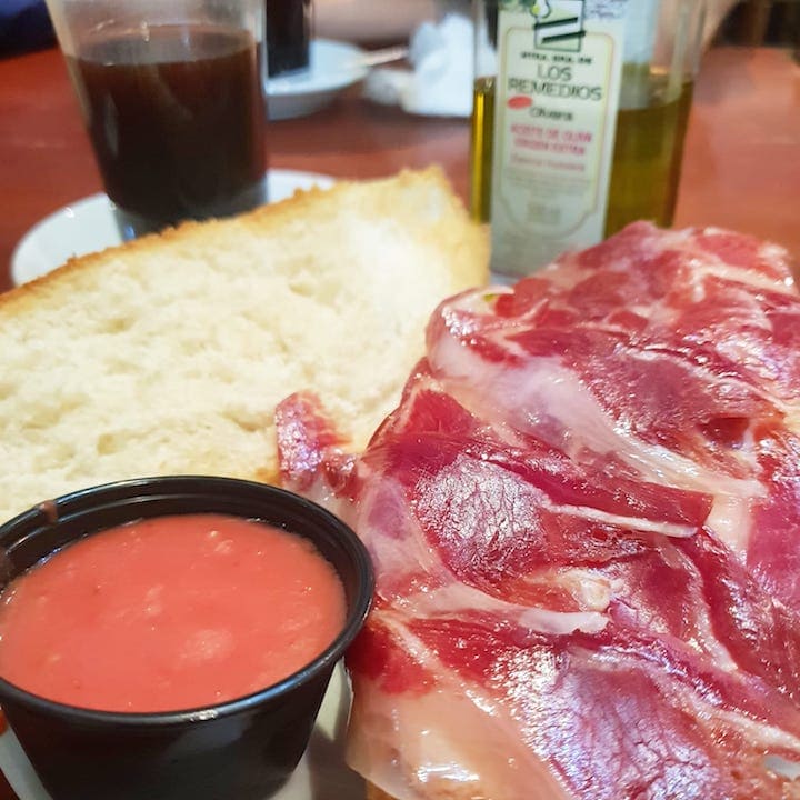 Close-up of toasted bread with cured ham, olive oil, and tomato purée on the side.