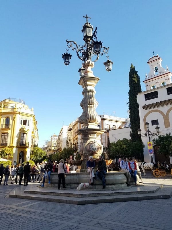 People sitting on an ornate fountain in the center of Seville