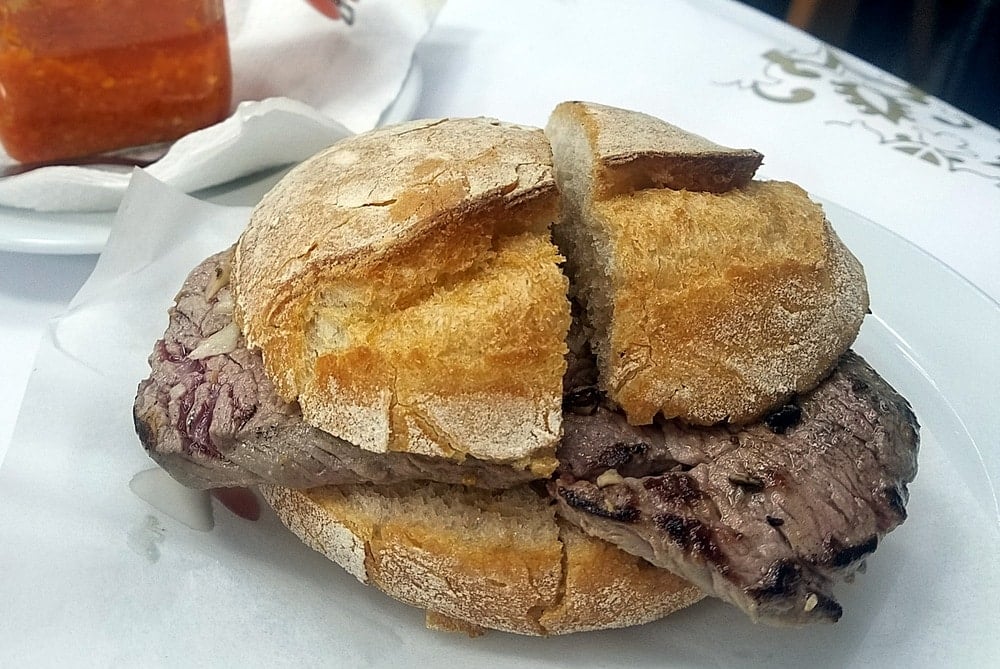 Close-up of a prego steak sandwich cut in half, sitting on a white plate.