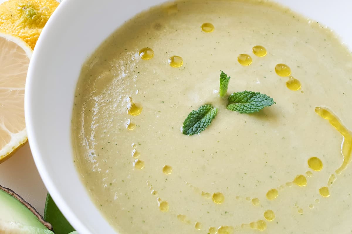 Close up of a bowl of green tomato gazpacho drizzled with olive oil and with a sprig of mint in the center.