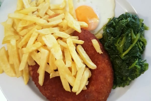 Close-up of a plate of fried alheira with french fries, a fried egg, and cooked greens.