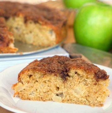 Close up of a slice of apple olive oil cake with the rest of the cake in the background