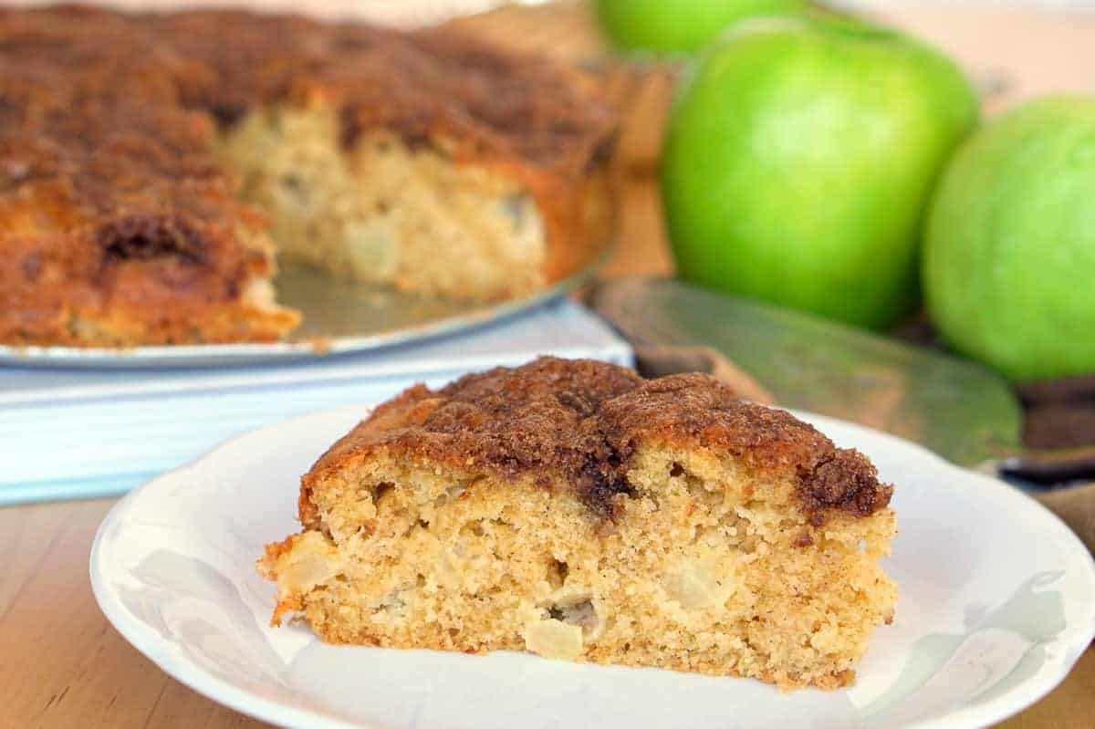 Close up of a slice of apple olive oil cake with the rest of the cake in the background