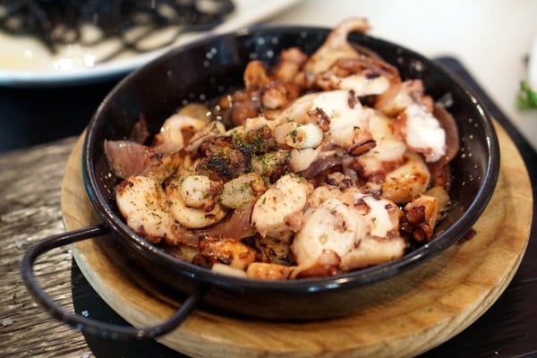 A round black dish of sliced and roasted octopus with herbs.