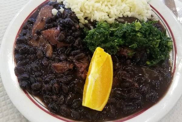 Close-up of a plate of feijoada, pork and bean stew with rice, greens, and lemon.