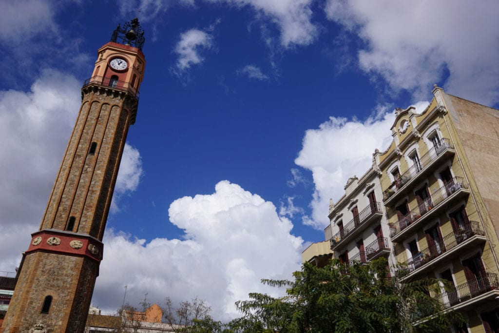 Blue sky with a stone clock tower on the left and historic building on the right.