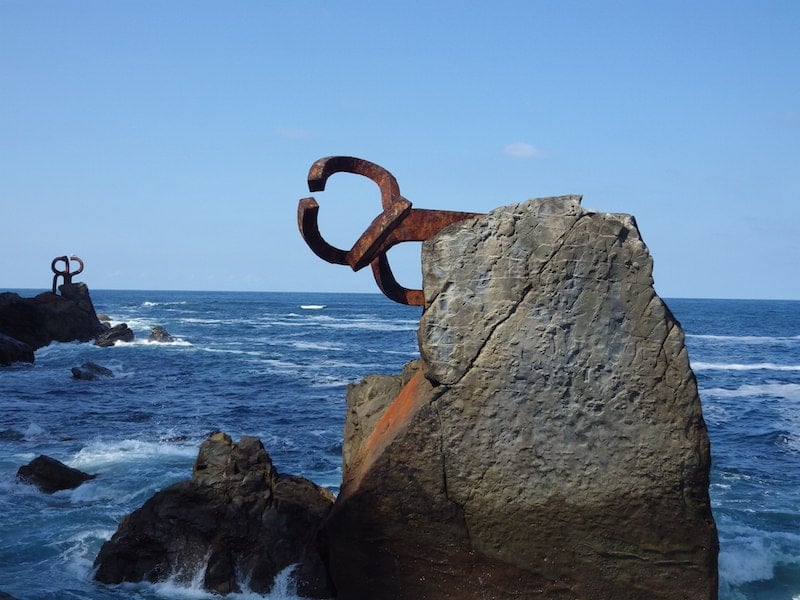 A rock in the sea with an abstract, rusted metal sculpture sticking out of it