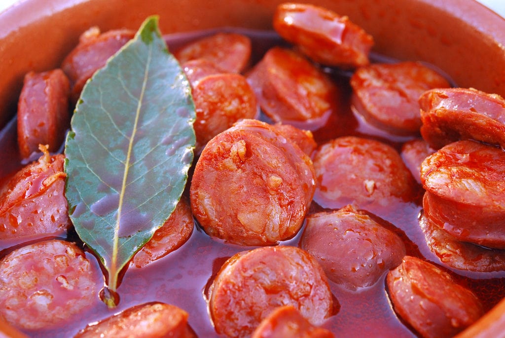 Close-up of sliced chorizo cooked in red wine with a bay leaf.